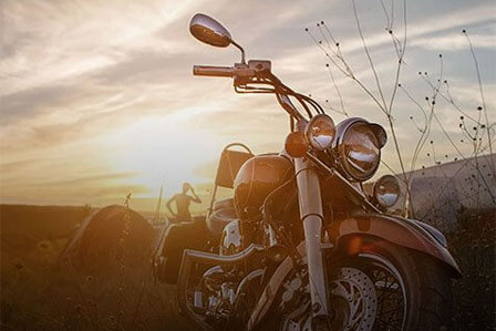 A close-up of a motorcycle's front section with the sunset in the background