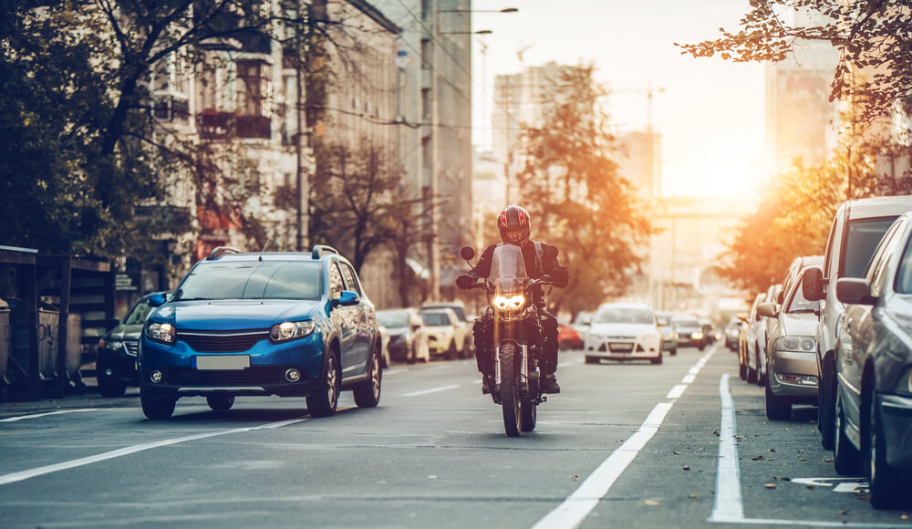 A motorcyclist riding during traffic hour on a city street, with cars lined up on one side