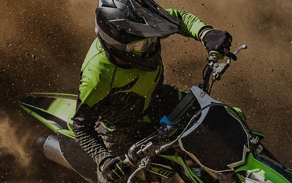 Motocross rider in lime green gear maneuvers a dirt bike, kicking up a trail of dust on a gritty track.