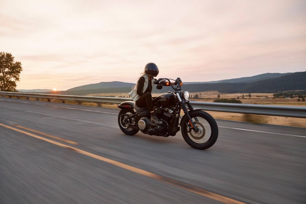 A woman rider on a cruiser motorcycle speeding along a highway at dusk on a rural landscape.