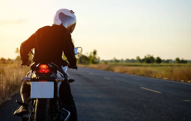 Motorcyclist with white helmet pauses and looks back on a rural road