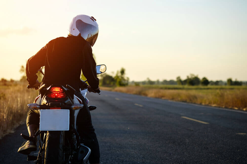 Motorcyclist with white helmet pauses and looks back on a rural road