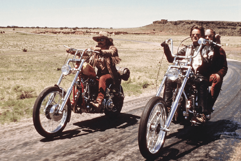 Two classic chopper motorcycles cruising on a country road with riders in vintage attire