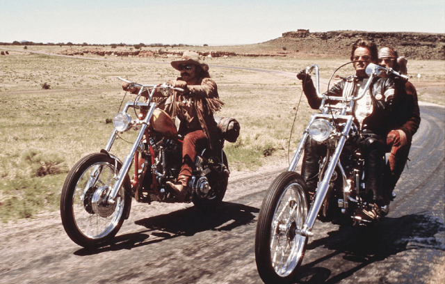 Two classic chopper motorcycles cruising on a country road with riders in vintage attire