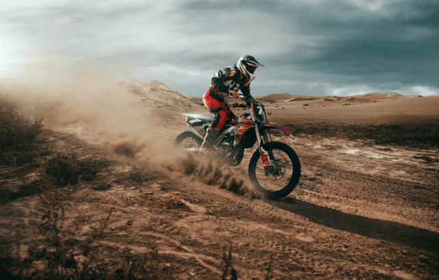 Motocross rider tackles a sandy trail with dust billowing behind