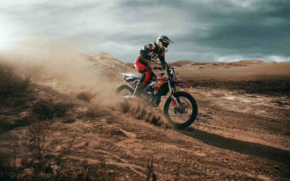 Motocross rider tackles a sandy trail with dust billowing behind