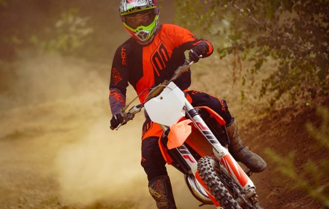 Motocross rider dressed in orange and black gear takes a sharp turn, kicking up dust.