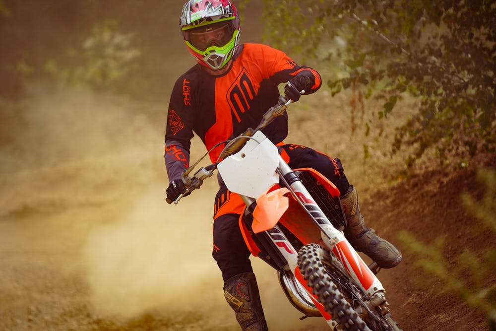 Motocross rider dressed in orange and black gear takes a sharp turn, kicking up dust.