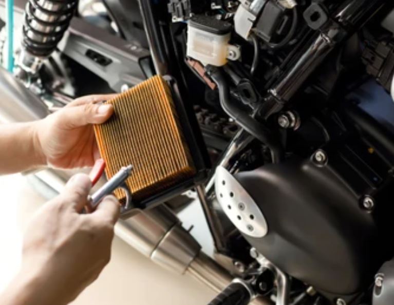 A mechanic is performing maintenance on a motorcycle, checking the air filter