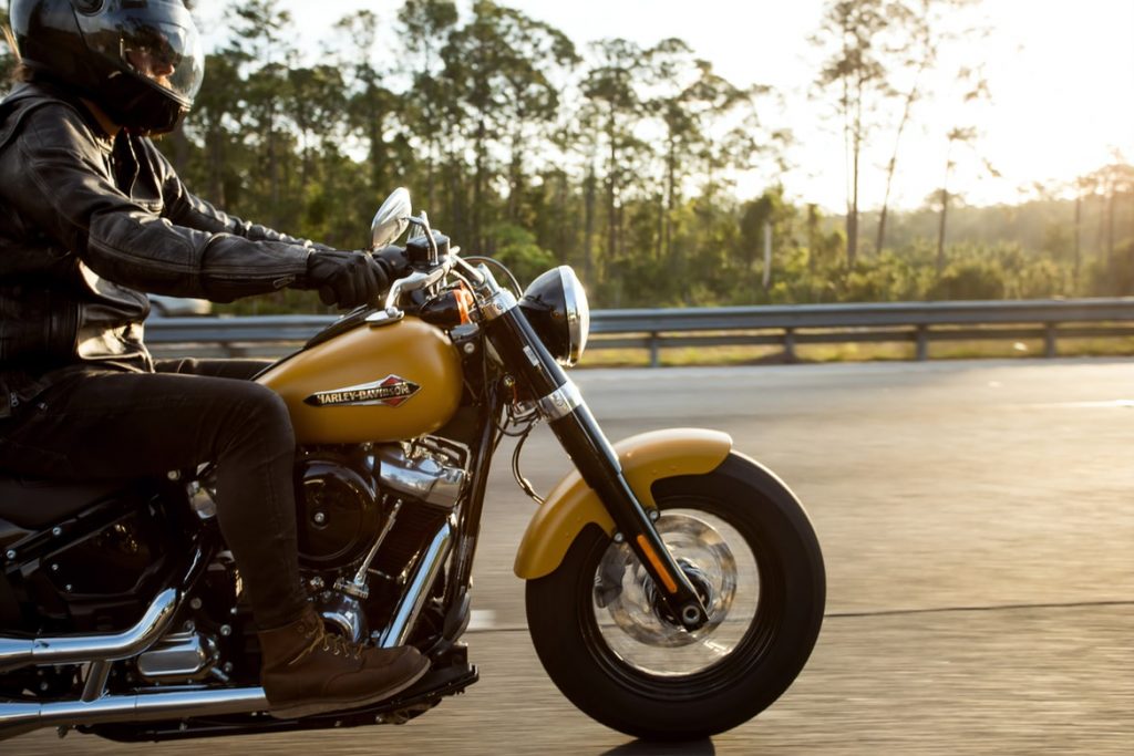 A motorcyclist in black attire riding a classic golden motorcycle on the highway