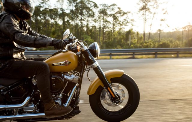 A motorcyclist in black attire riding a classic golden motorcycle on the highway